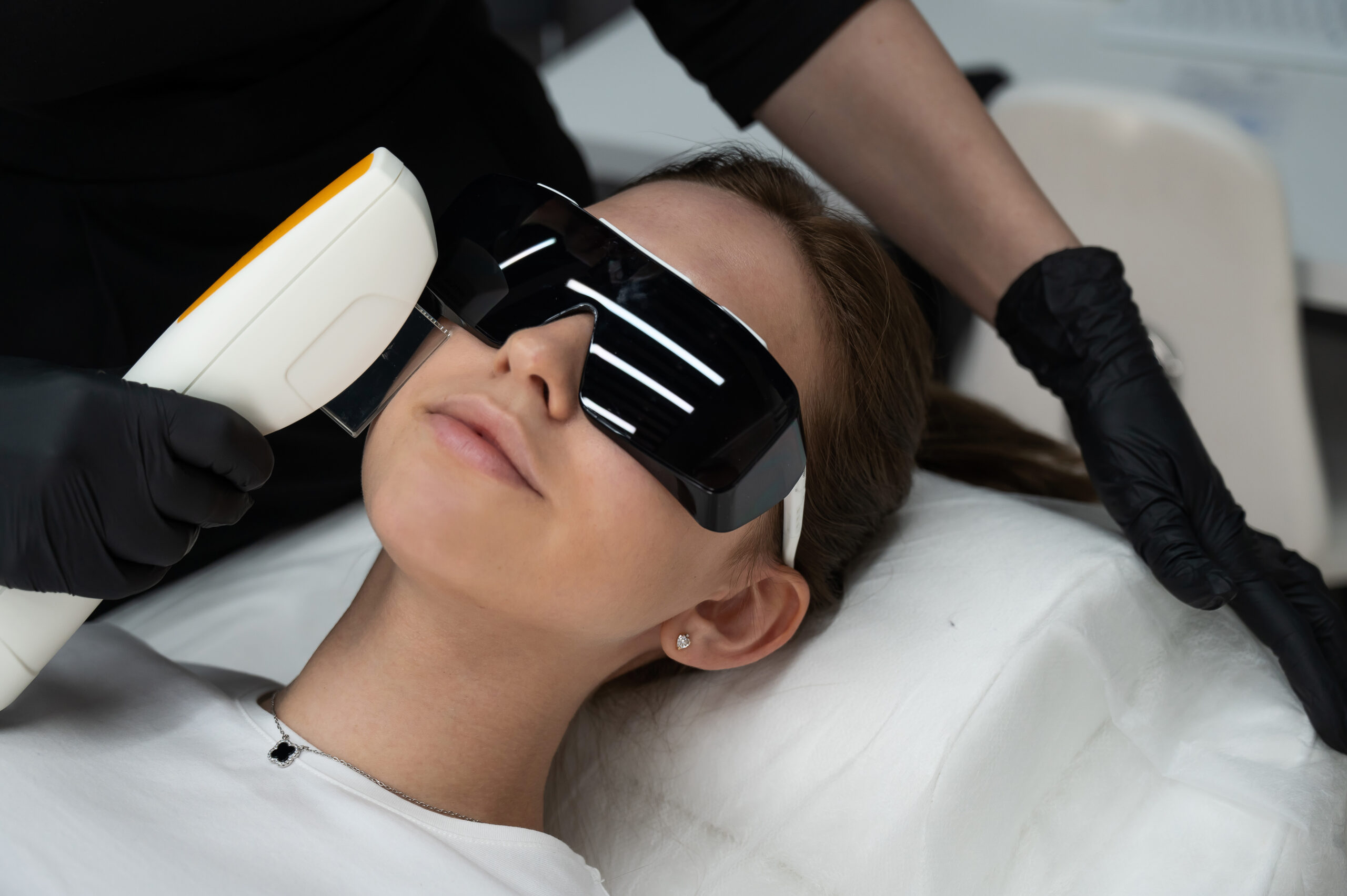 Young caucasian woman in goggles on photorejuvenation procedure. Portrait of a girl in a beautician's clinic