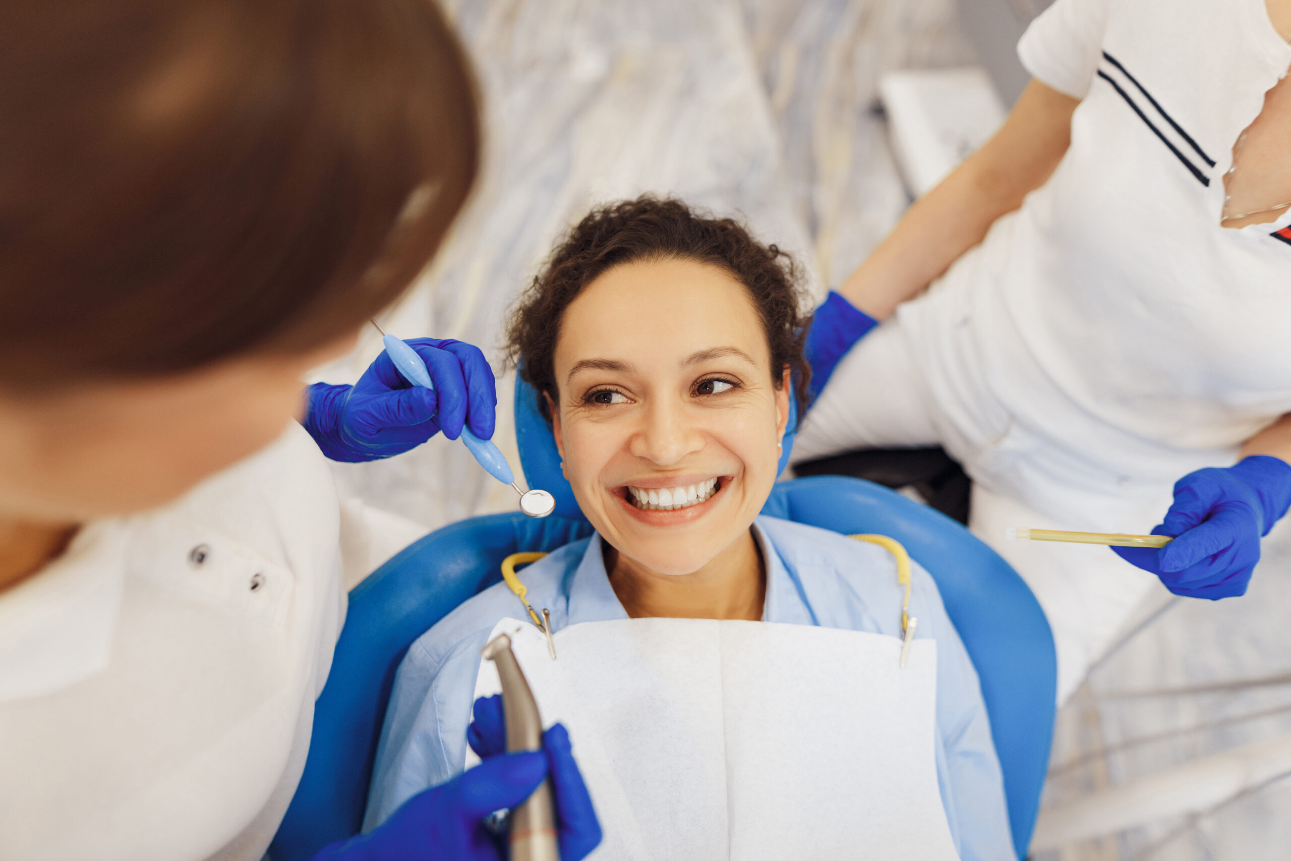 Top view of smiling female client sitting in dental chair, looking at dental doctor with tools