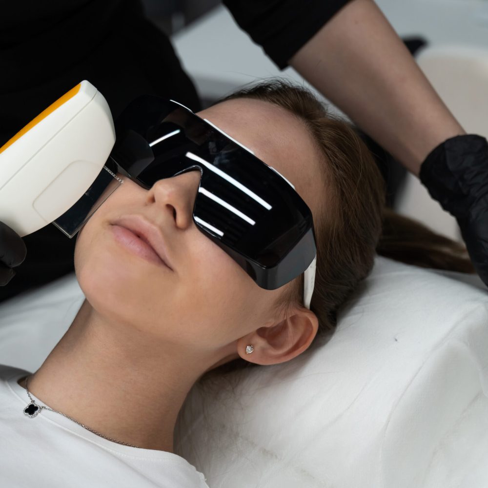 Young caucasian woman in goggles on photorejuvenation procedure. Portrait of a girl in a beautician's clinic