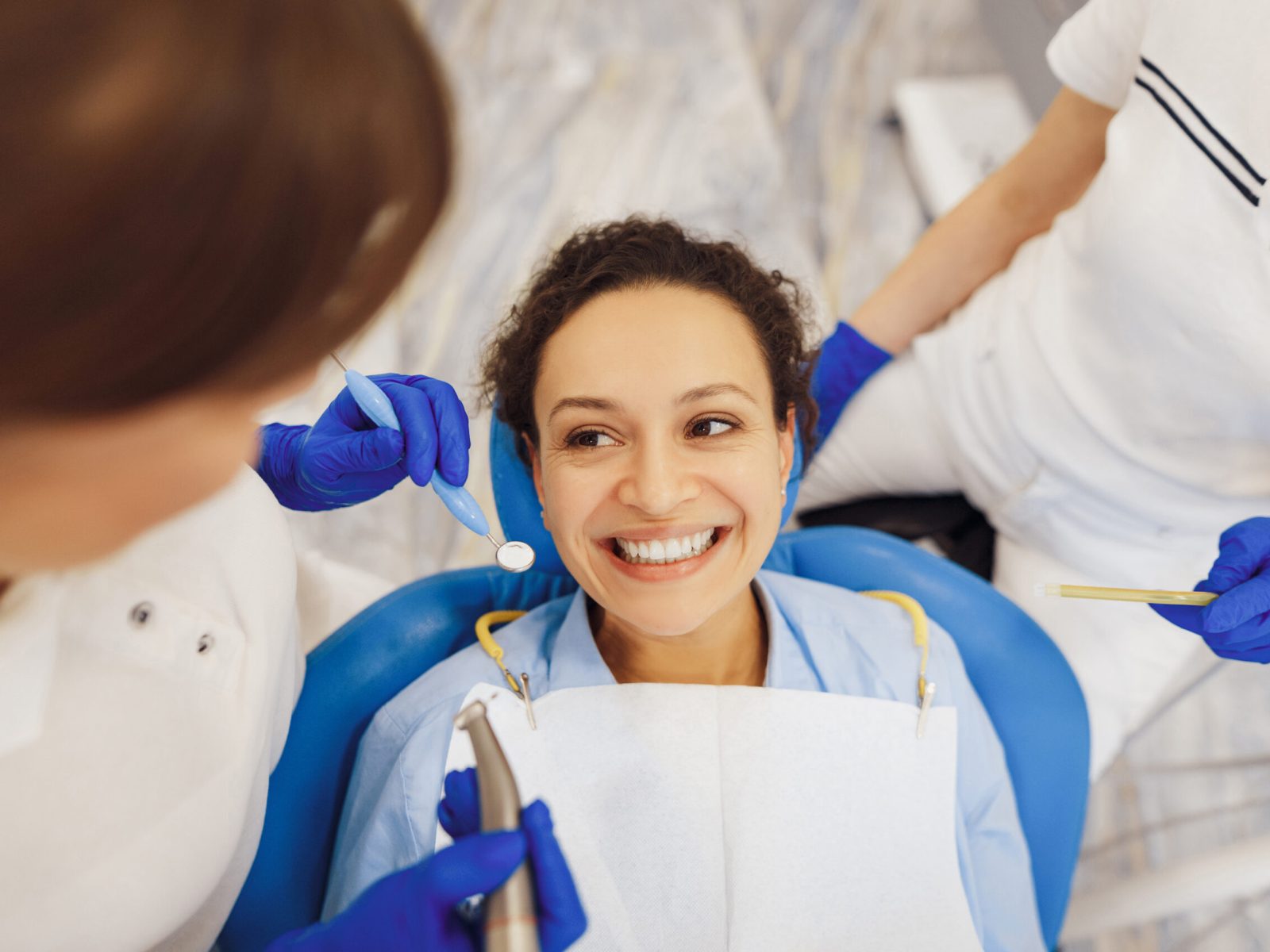 Top view of smiling female client sitting in dental chair, looking at dental doctor with tools